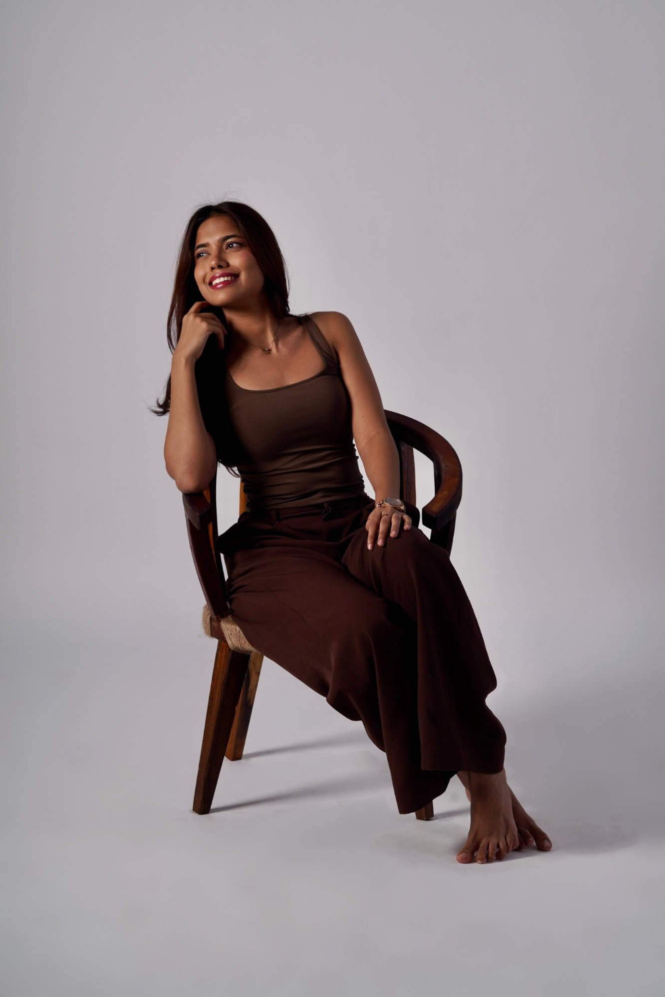 Aarohi smiling, seated on Chair 03, a wooden armchair with a jute seat