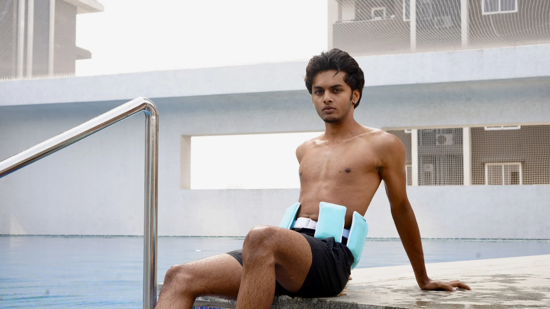 A man sitting at the edge of a rooftop pool wearing the Ascend belt