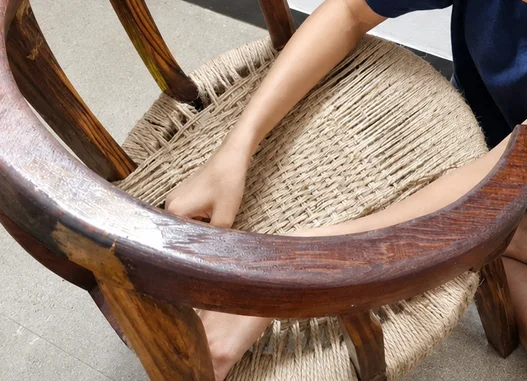 Hands weaving jute rope across the seat