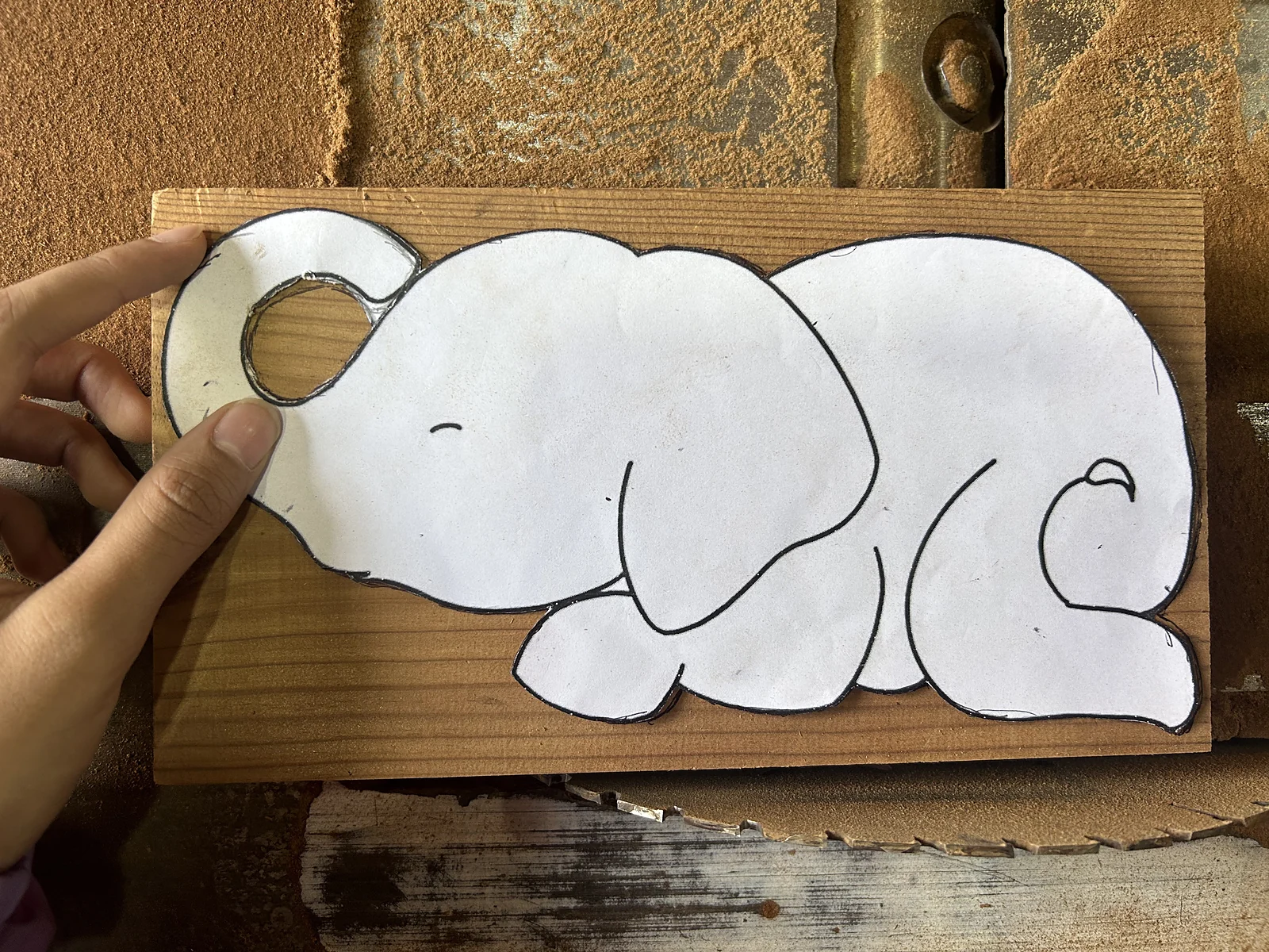 A paper template of Ellie held against a pine board in the workshop