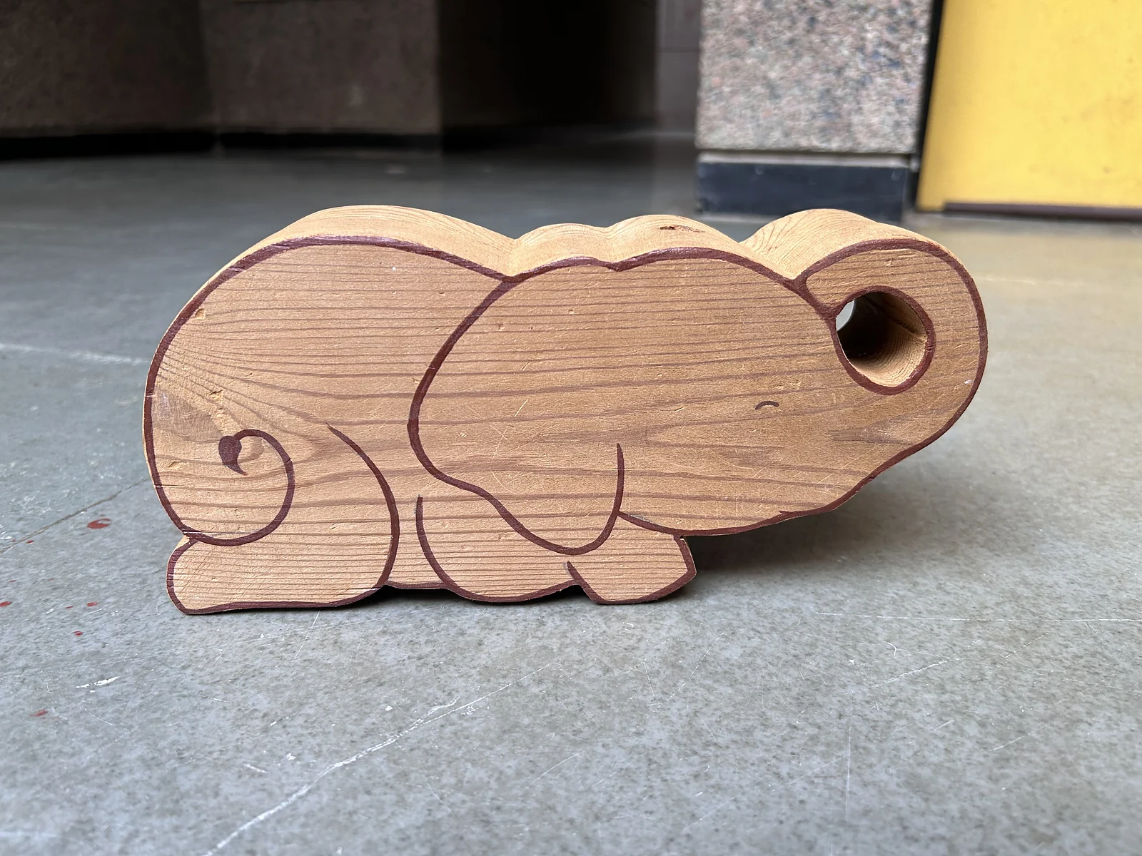 The finished wooden elephant with its painted outline, on a stone floor, unretouched